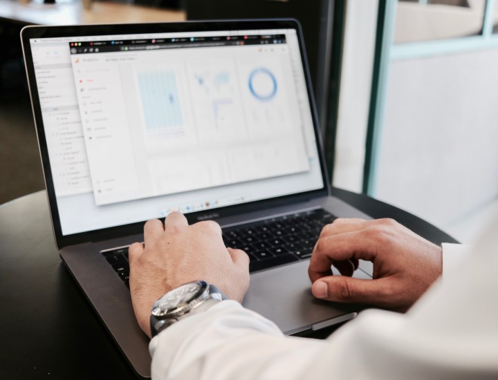 Mans arms/hands on laptop, blurry screen with data analytics.